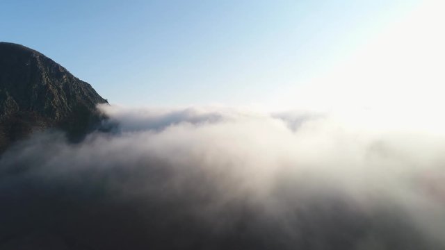 Beautiful view of high mountain top surrounded by dense layer of clouds against blue sky and bright sun. Shot. Mountain landscape