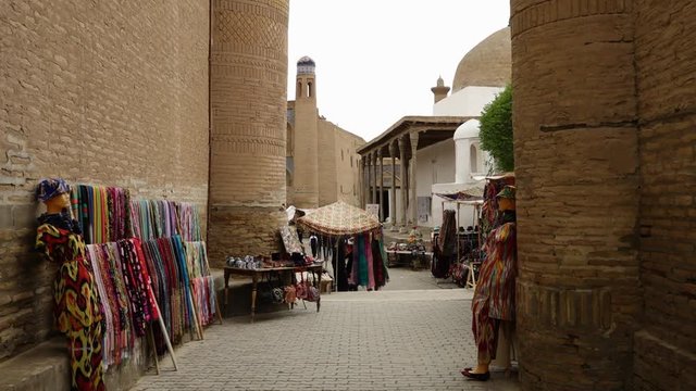 A wide view of an alley in the mosaic temple complex of Xiva, Uzbekistan, with merchant tables and a mannequin displaying clothes and merchandise
