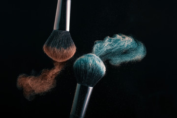 Cosmetic shades of different colors, red and blue, fly away from two make-up brushes creating a...