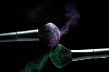 cosmetic shades of different colors, lilac and green, fly away from two makeup brushes creating a...