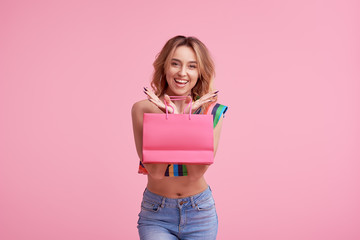 Satisfied buyer. Portrait of an excited happy girl wearing colorful summer clothes holding shopping bag isolated over pink background.  Place to sign or text  on the package. Sale concept