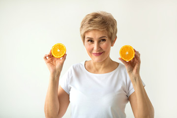 beautiful aged woman with a short haircut in a white T-shirt with oranges in her hands on a white background