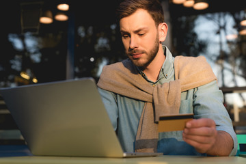 handsome man holding credit card while using laptop