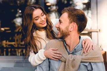 Fototapeta premium cheerful girl hugging and looking at handsome bearded boyfriend
