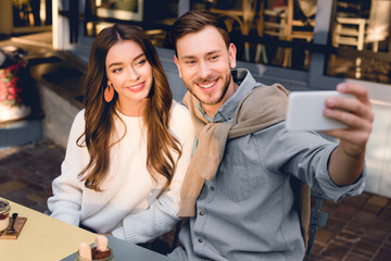 selective focus of handsome man taking selfie with cheerful girl