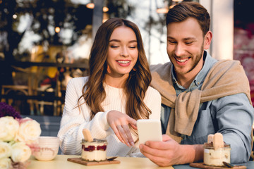 cheerful man sitting with happy girl pointing with finger at smartphone