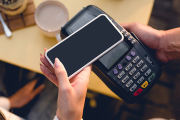 cropped view of young woman paying with smartphone in cafe