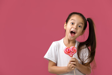 Beautiful cute little child girl with sweet candy lollipop isolated on pink background