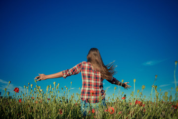Obraz na płótnie Canvas Poppy field. A girl with long hair jumps in a meadow among flowers