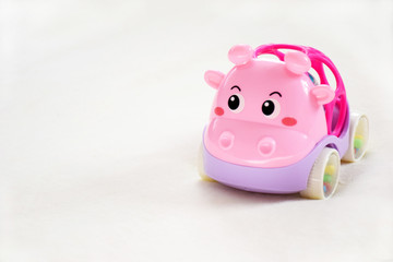 Interesting bright toy pink rattle on a white background with copy space. Pink fun car close up with selective focus.