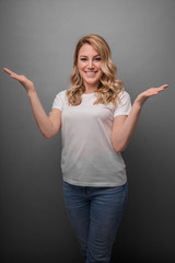 Beautiful blonde is smiling and shows fingers in different directions. Studio photo of a young attractive woman on a gray background.