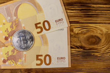 Fifty euro banknotes and silver bitcoin on wooden background. Top view