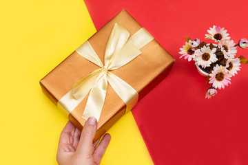 Female hands holding present with yellow bow on red, yellow paper . Festive backdrop for holidays: Birthday, Valentines day, Christmas, New Year. Flat lay style