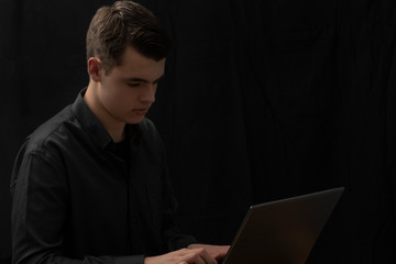 Handsome young businessman seen from the right  typing on his laptop. Black background.