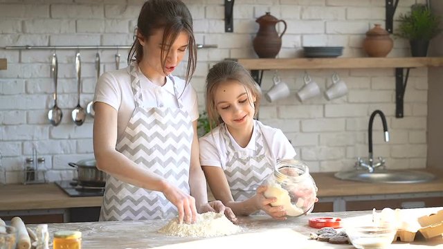 Sister preparing dough. Younger sister pouring flour in the dough on the kitchen table.
