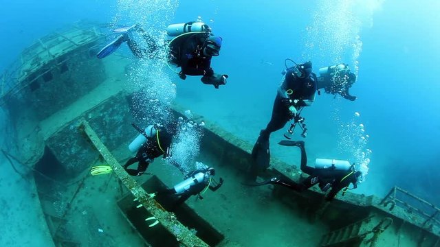 Group of divers swims near ship wreck underwater. Sunken ship covered in coral on Pacific Ocean seabed in Fiji.