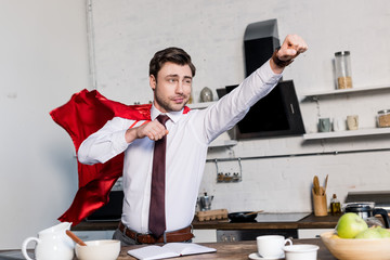 cheerful man in superhero red cloak posing in kitchen at home