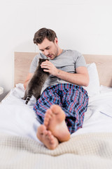 selective focus of handsome man in plaid shirt lying in bed with cute raccoon