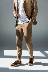 partial view of trendy man in beige suite standing in sunlight on grey