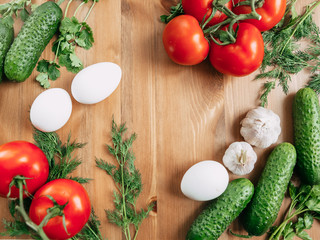 Frame of tomatoes and cucumbers, with greens and garlic, eggs on a wooden texture