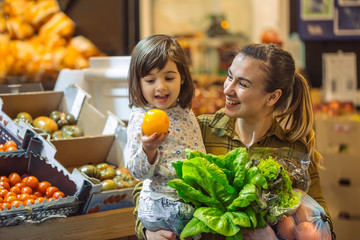 Family in the supermarket. Beautiful young mom and her little daughter smiling and buying food.