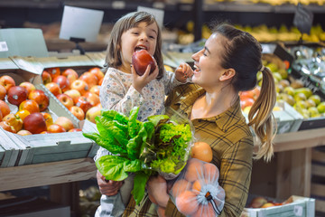 Family in the supermarket. Beautiful young mom and her little daughter smiling and buying food.