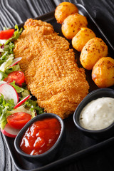  main course of cod fillet in breading with a garnish of new potatoes and fresh vegetable salad close-up on a plate on the table. vertical