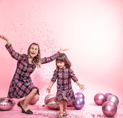 Funny mom and child on a pink background. Little girl and mother having fun with balloons and confetti