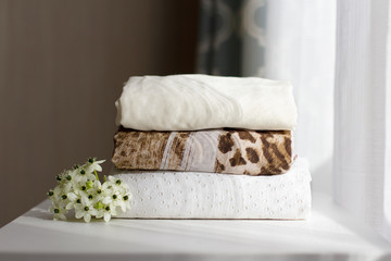 a stack of neatly folded clothes made of natural fabrics decorated with a white flower in the sunlight