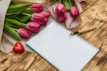 Notepad with tulip bouquet on wooden background top view