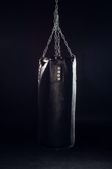 Leather punching bag hanging on steel chains on black