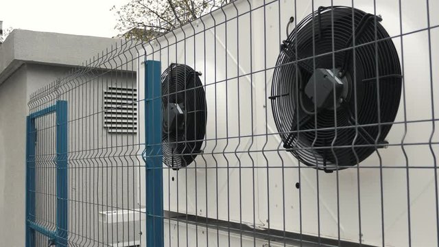 Heating ventilation and air conditioning outdoor units for office and mall buildings guarded by a big fence behing of a commercial building.