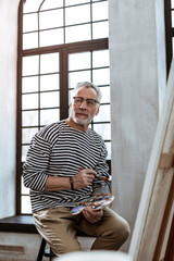 Mature experienced artist sitting near window in his workshop