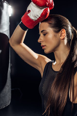Tired boxer with ponytail standing near punching bag on black