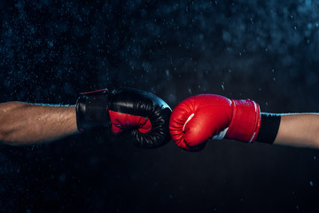 Partial view of two boxers in boxing gloves touching hands on black