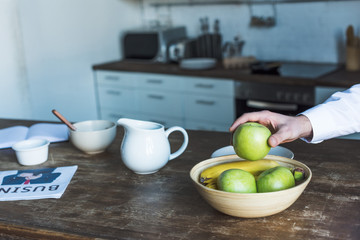 partial view of man taking apple from bowl on wooden kitchen table