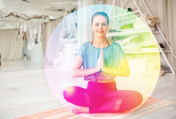 mindfulness, spirituality and healthy lifestyle concept - woman meditating in lotus pose at yoga studio over rainbow aura - obrazy, fototapety, plakaty