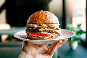 huge appetizing juicy Burger with bacon, beef cutlet, fresh salad, tomatoes, onions, sauce, cheese and black fresh bun with sesame seeds