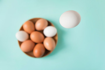 White egg falls in a wooden plate with eggs on a blue table. Happy Easter. Selective focus. Top view