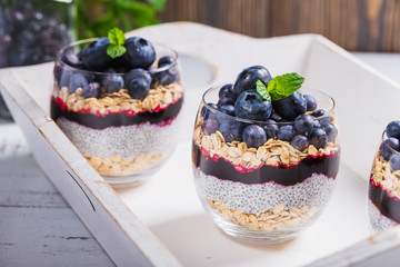 Light dessert of chia pudding with blueberry, oats and fresh jam, served in thin glass.