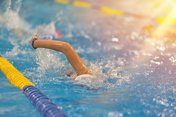 Young boy in swim suit, goggles and cap swimming in the blue water pool