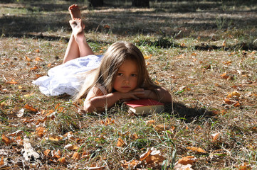 Fototapeta premium Cute girl lying on the ground in the park and read the book.autumn mood. Soon to school