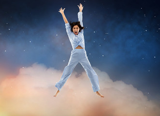 Fototapeta na wymiar fun, people and bedtime concept - happy young woman full of energy in blue pajama jumping over starry night sky background