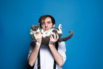 handsome man holding on back cute gray cat near face and smiling on blue background with copy space