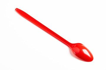 A single long and unused shiny red plastic spoon deliberately and artistically set on a plain white background.