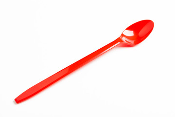 A single long and unused shiny red plastic spoon deliberately and artistically set on a plain white background.