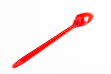 A single long and unused shiny red plastic spoon deliberately and artistically set on a plain white background.