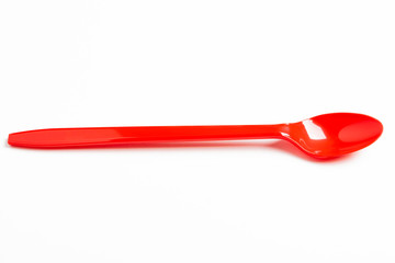 A single long and unused shiny red plastic spoon deliberately and artistically set on a plain white background.