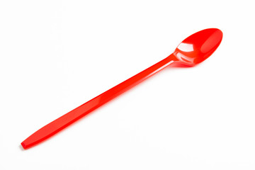 A single long and unused shiny red plastic spoon deliberately and artistically set on a plain white background.