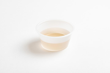 A fresh urine sample in a small round plastic cup container set on a plain white paper background.